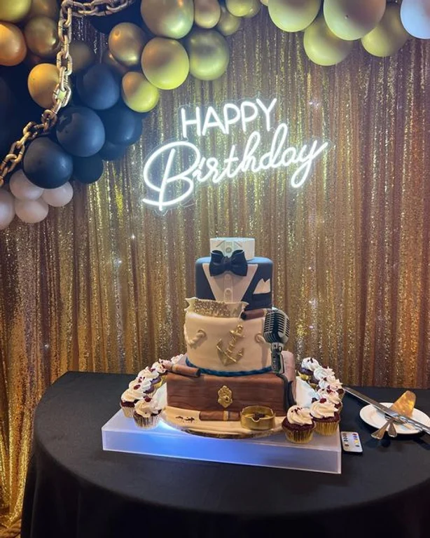A birthday cake with a bow tie and suitcase on top.