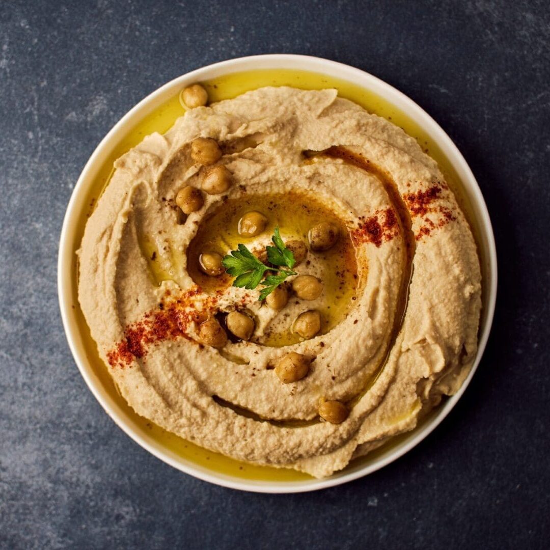A bowl of hummus with some nuts and herbs.
